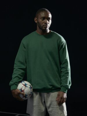 Studio portrait of an African American man in a green sweatshirt holding a soccer ball.